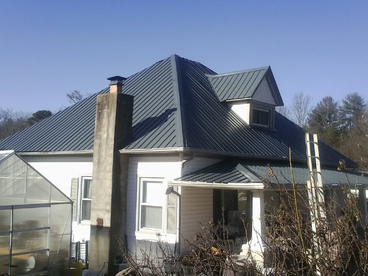 Dark blue standing seam metal roof on a white farmhouse with dormer — Slate & Tile Roof Repair by Roofing Brothers in Red Oak