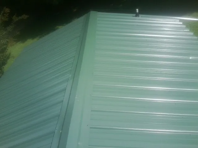 New green metal panels meeting at the ridge of a roof — Flat Roof Repair work by our crew in Red Oak