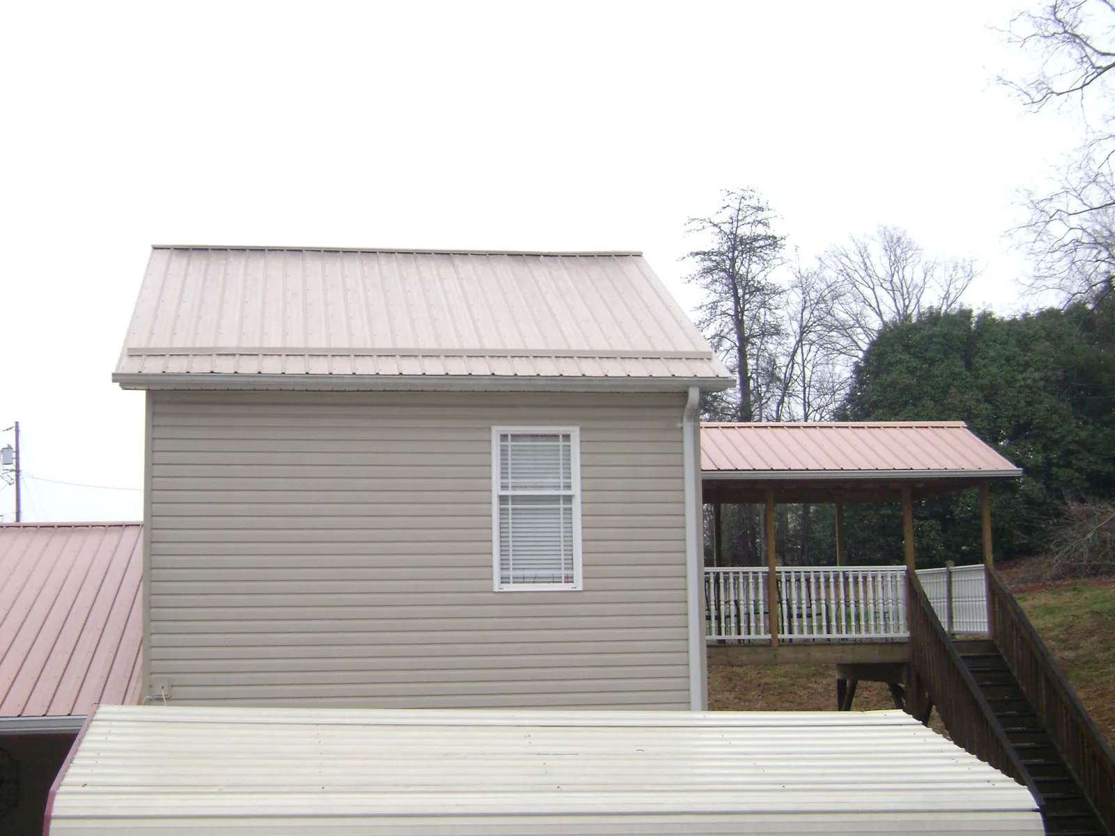 Tan metal roofs on a two story addition and attached porch, from a Roof Replacement job in Red Oak